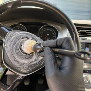 Detailreinigung eines Lenkrads im Fahrzeug mit einem Pinsel bei der Innenraumaufbereitung